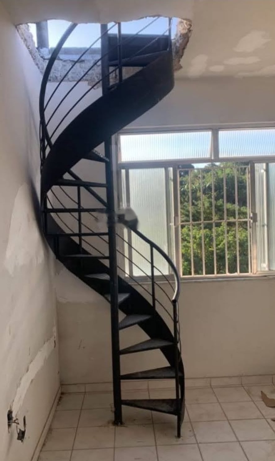 Escada caracol de ferro preta com chapa lateral, instalada dentro de casa